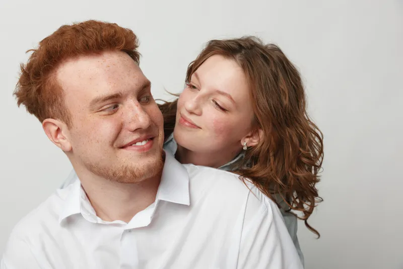 Happy young couple with red hair and curly hair smiling and looking at each other on white background. Concept of love, relationship, friendship, and positive emotions between people.