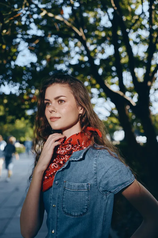 young woman with red scarf outdoors in summer sunlight surrounded by green trees and casual clothing enjoying nature and warmth