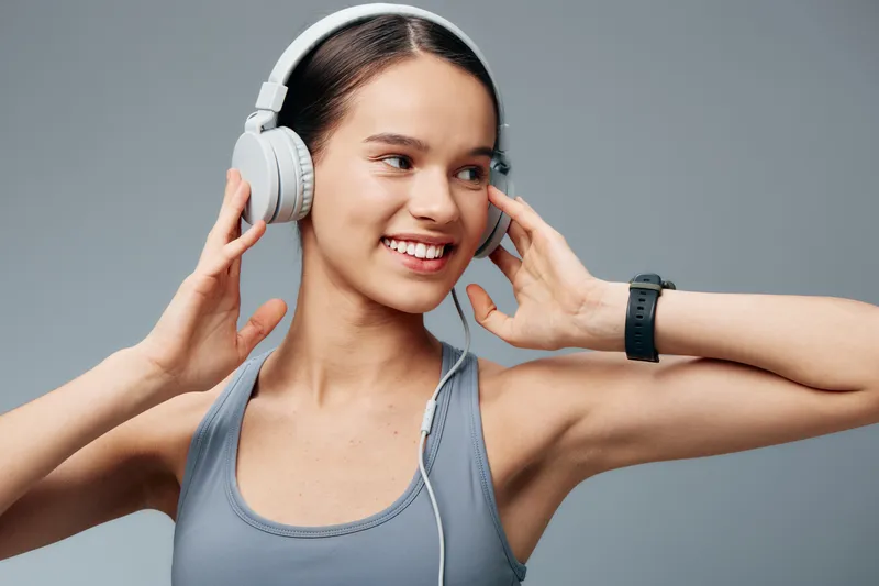 Woman fitness and sport scene, smiling as she wears headphones during a workout, energetic pose in gym wear, emphasizing rhythm, focus, and motivation.