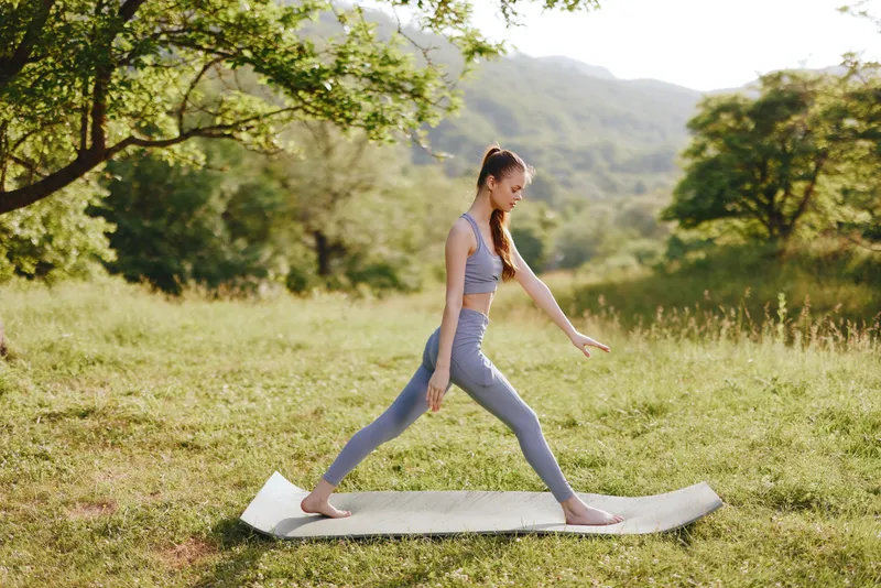 Young woman practicing yoga outdoors on a mat in a lush green field, showcasing strength and tranquility, perfect for wellness and fitness themes