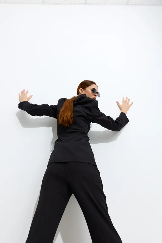 fashion woman dressed in stylish black outfit and sunglasses posed against white wall with modern and minimalistic vibe, showcasing confident and bold look
