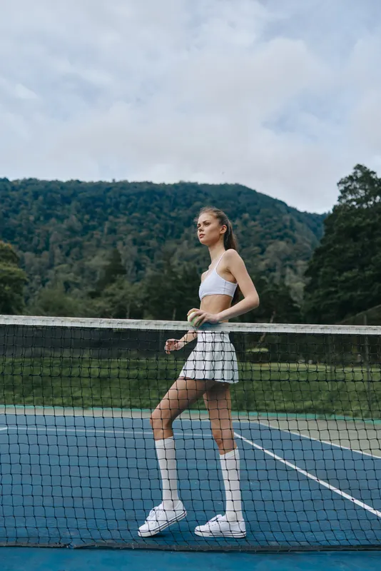 Athletic young woman in a sporty outfit on a tennis court, showcasing confidence and determination in a serene outdoor environment among greenery