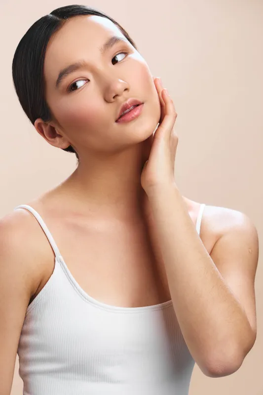 Asian woman with a serene expression rests her face on her hand against a light backdrop, conveying calm confidence and poised beauty suitable for lifestyle campaigns.