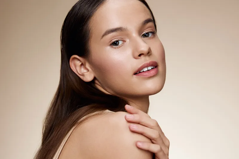 Young woman with smooth skin showcasing natural beauty and elegance against a soft, neutral background, emphasizing skin care and wellness