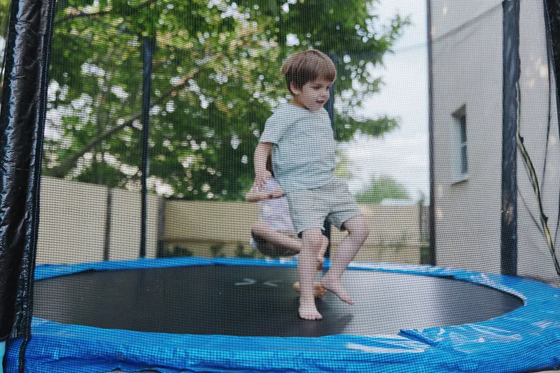 Happy boy bouncing on a trampoline, enjoying outdoor playtime, vibrant summer atmosphere, and playful energy radiating in a sunny setting.