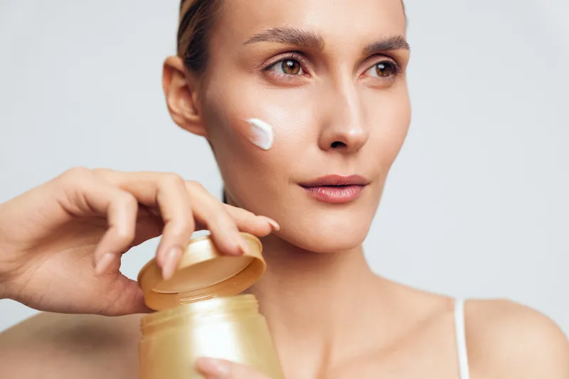 Closeup of woman applying face cream on cheek, skincare routine, natural skin texture, soft lighting, neutral background, focused expression, beauty concept