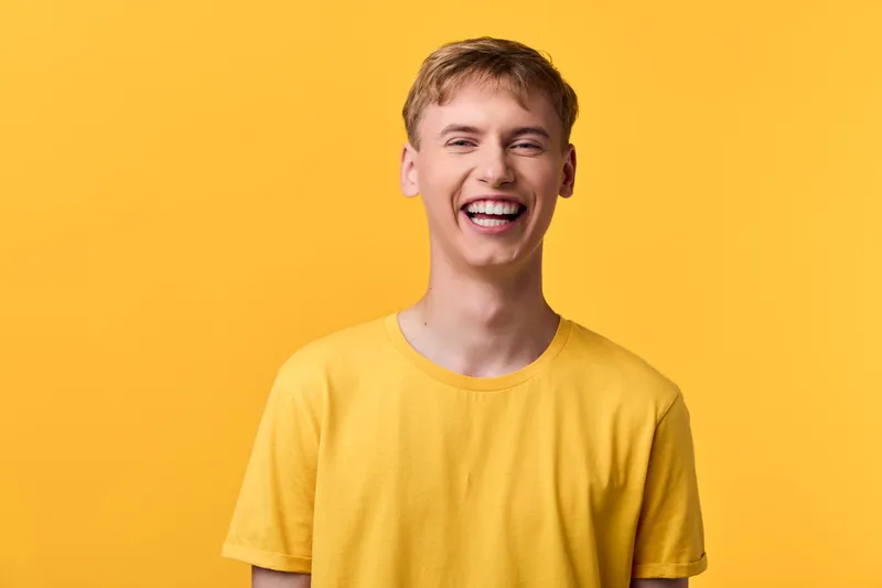 Cheerful man wearing a yellow tee smiles against a bright yellow backdrop, conveying happiness, optimism, casual style, friendly energy, and a sunny mood for lifestyle or fashion use