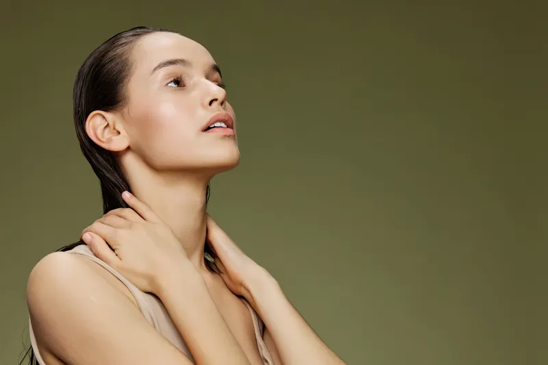 Young woman with wet hair in natural light, showcasing a serene expression against a green background, embodying beauty and confidence