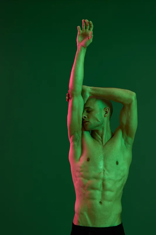 Athletic man posing with striking green lighting, showcasing strong physique and dynamic expression, emphasizing confidence and power in a unique artistic setting.