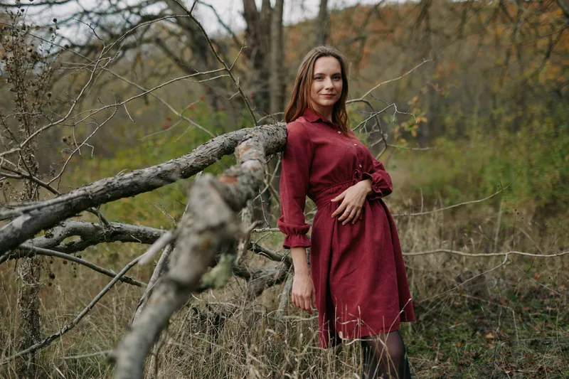 Candid portrait of a woman in a red dress leaning on a fallen tree in a rural meadow, natural light and subtle textures highlight a genuine expression, authenticity and credible storytelling.