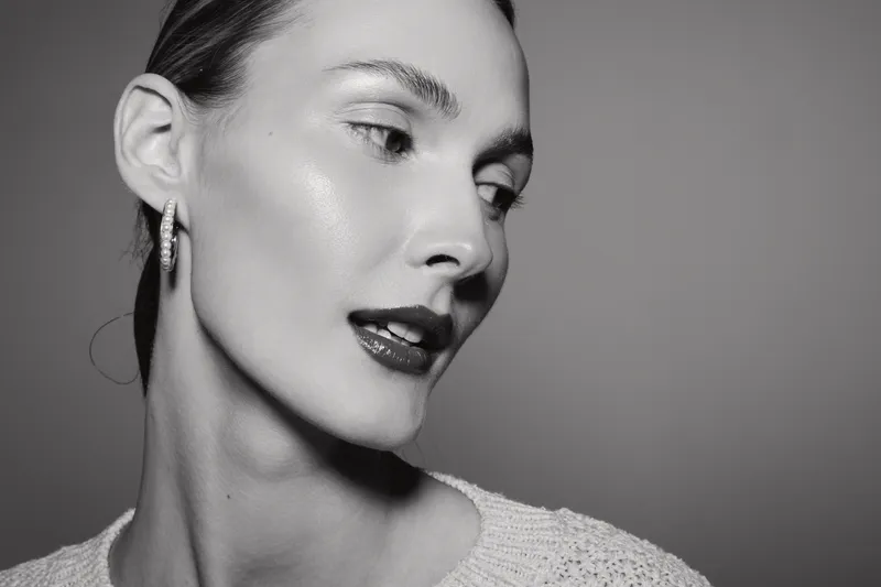 Close-up black and white portrait of a light skinned Caucasian woman with slicked back hair and earrings looking to the side. Concept of elegance, beauty, and fashion.