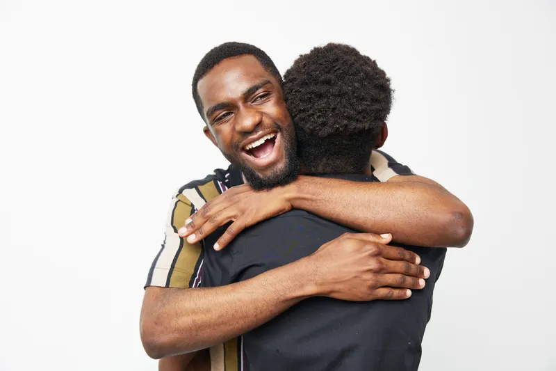 Happy black man embracing a friend, showcasing warmth, friendship, and joy in an uplifting moment. A bright, cheerful expression enhances the positive vibe of the scene.