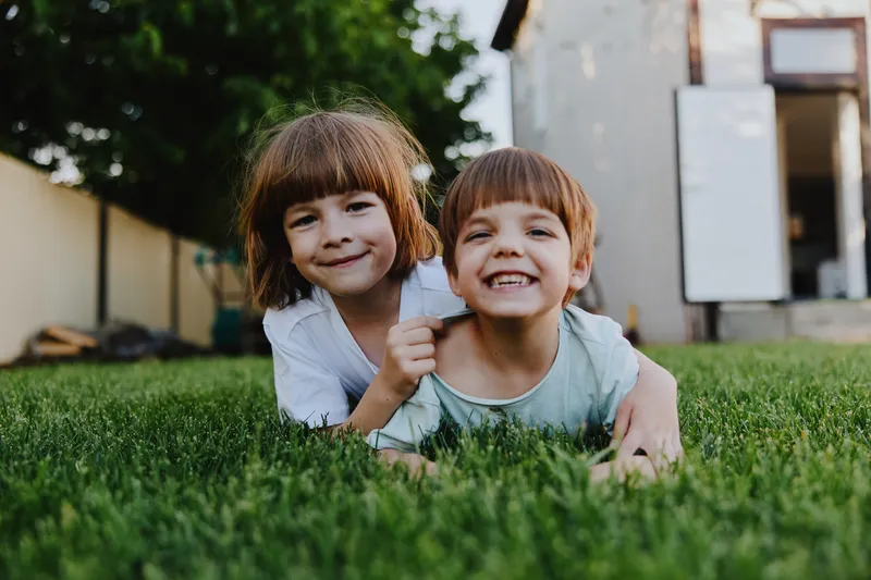 Happy children playing together on lush green grass in a sunny backyard, showcasing friendship, joy, and playful spirit in a vibrant outdoor setting.
