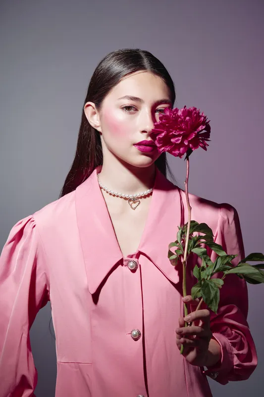 Young woman with flawless makeup holds a pink peony dressed in a stylish pink outfit in creative fashion photography. Concept of beauty, elegance, and sophistication.
