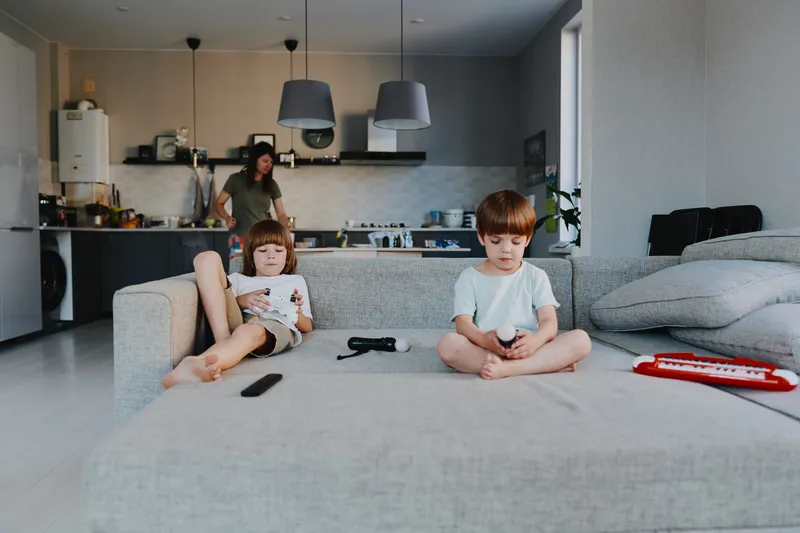 A caring woman supervises her children, who are engrossed in their activities, creating a warm and cozy atmosphere in a modern living space.
