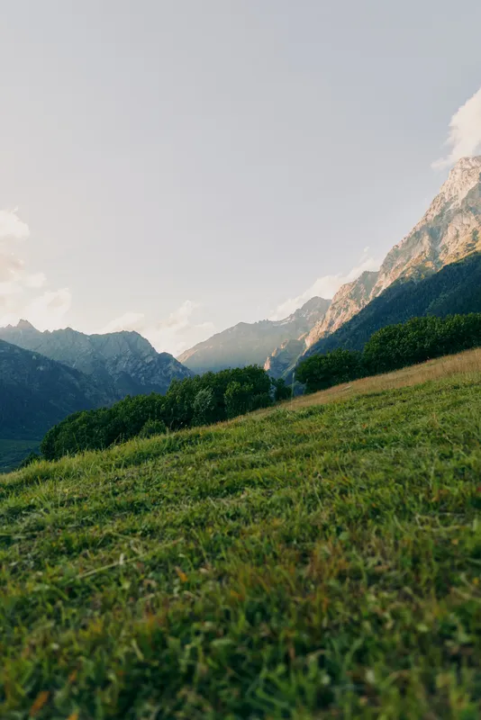 Woman lifestyle concept with a person standing on a grassy hill, surrounded by lush greenery and mountains under a clear sky, peaceful outdoor scene.