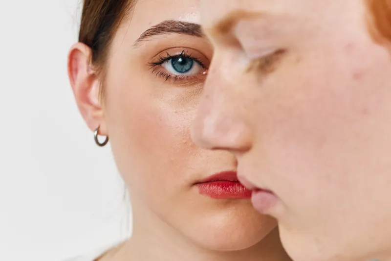 Closeup portrait of woman and man with serious expressions for emotion, relationship, and connection, skin details, and eye contact in studio with white background and natural light.