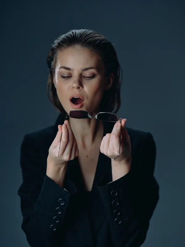 surprised woman holding sunglasses with dark background and stylish black outfit