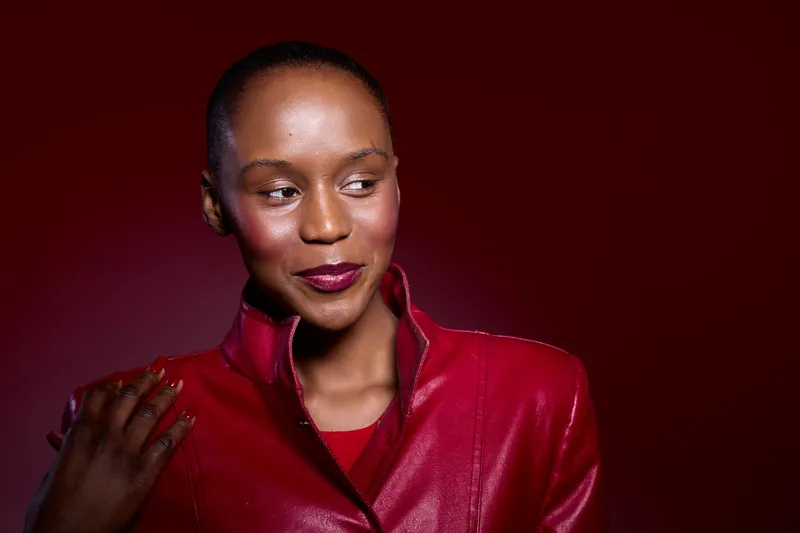 Portrait of a confident African woman with dark skin wearing a red leather jacket against a dark red background. Concept of fashion, elegance, and beauty with studio lighting.