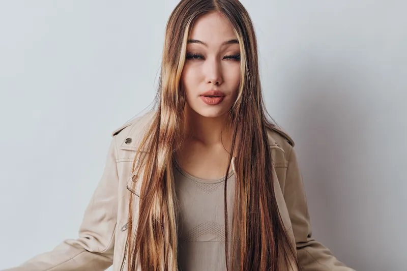 Young woman with long straight hair posing with eyes closed in casual clothes against white background in studio. Fashion, portrait and beauty concept with natural look.