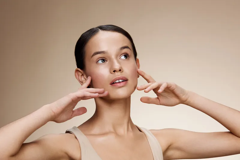 Elegant young woman with a natural makeup look, expressing serenity and beauty against a soft beige background This image captures grace and confidence