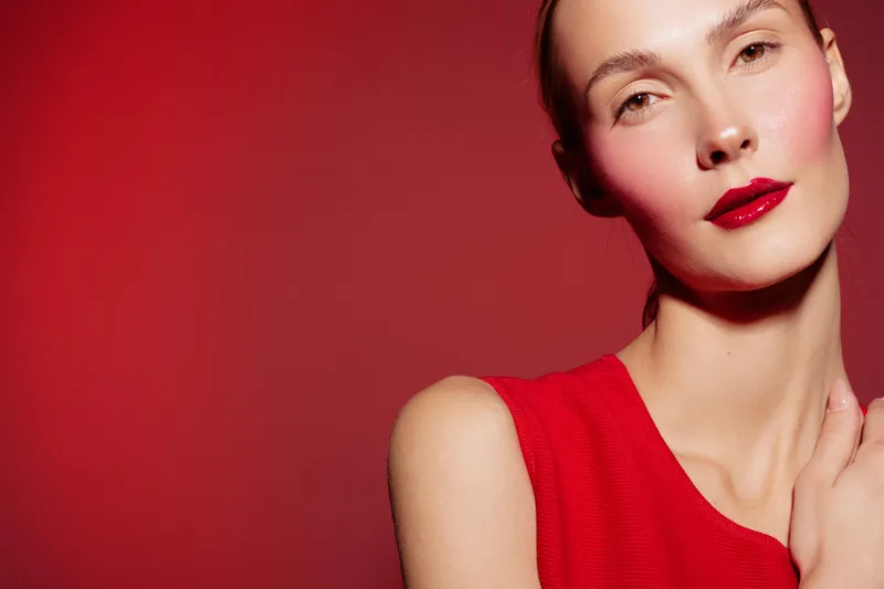 Close-up of a woman with red lipstick and red dress against red background. Concept of beauty, fashion, makeup, and elegance with vibrant color contrast.