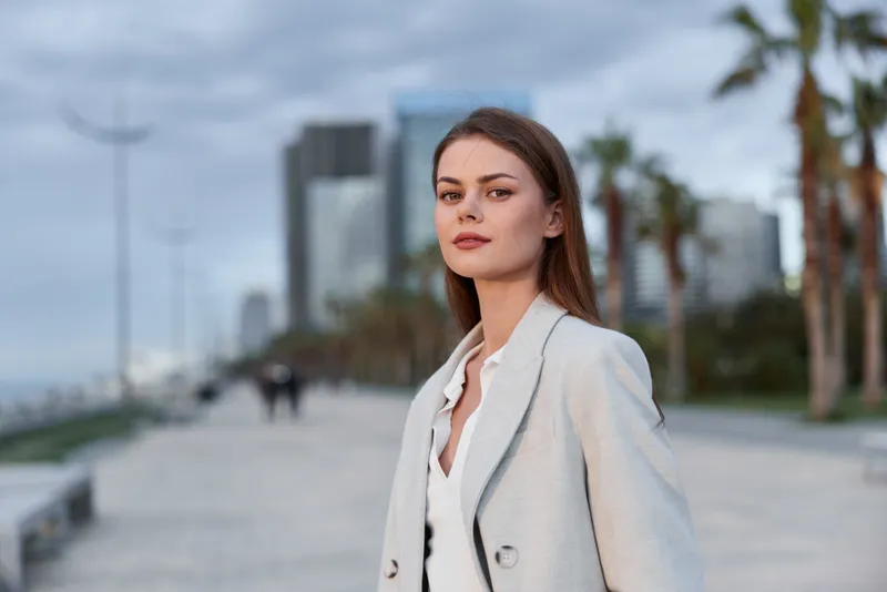 Confident business woman in a light suit standing outdoors with a city skyline backdrop, exuding professionalism and poise, perfect for business themes.