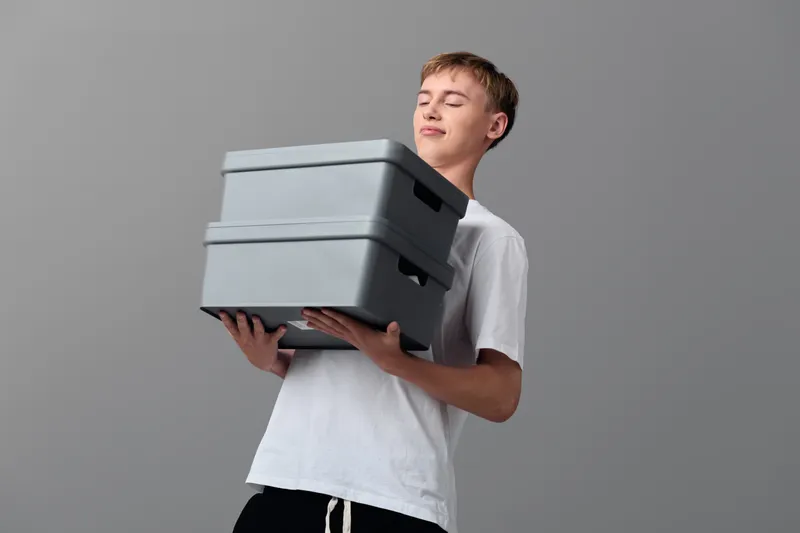 Boxes, stack, boy, carrying, storage, moving, load, delivery, casual scene showing a teen lifting grey containers in a simple studio setup, focusing on motion and everyday tasks