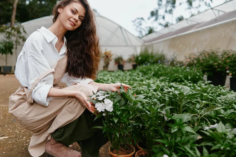 Young woman in a garden holding white flowers, showcasing a cheerful expression amidst lush greenery, perfect for eco friendly and gardening concepts