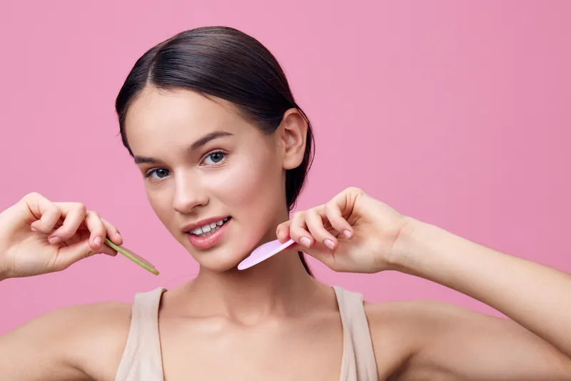 Young woman with smooth skin holding beauty tools, showcasing skin care routine in a vibrant pink background, ideal for wellness and beauty themes