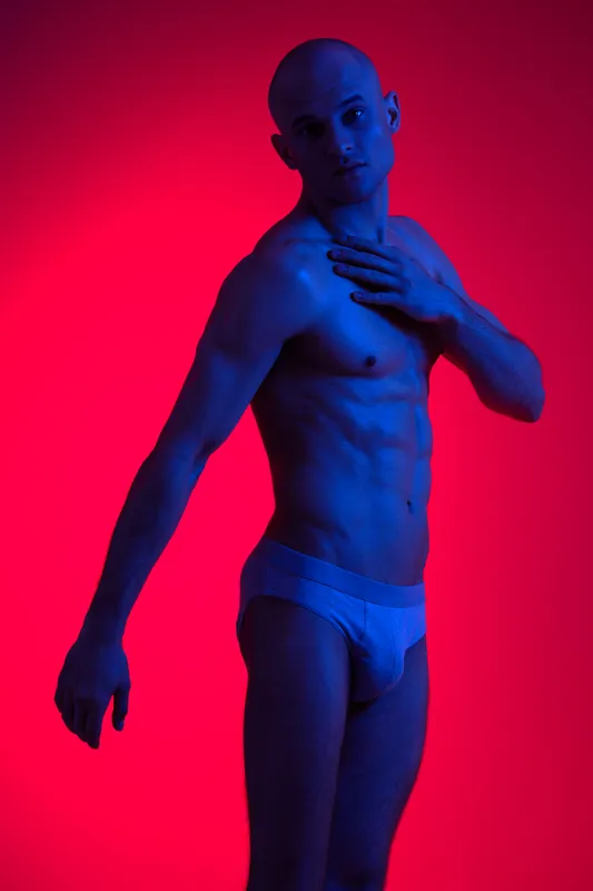 Male model posing dramatically against a vibrant red background, showcasing a strong physique and unique lighting. This captivating image inspires bold artistry and expression.