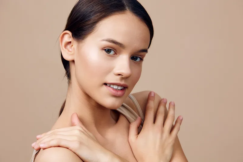 Young woman with natural makeup and light skin tone against a beige background, showcasing healthy skin and a confident expression