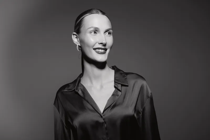 Portrait of a smiling Caucasian woman with pale skin wearing a satin shirt looking away, studio black and white photography.