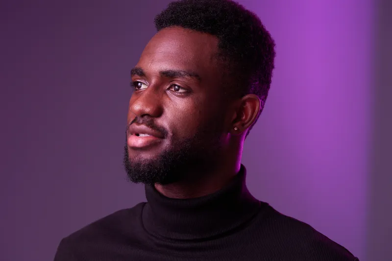 Confident African man in a black turtleneck sweater, showcasing a thoughtful expression against a vibrant purple background, conveying self assurance and elegance