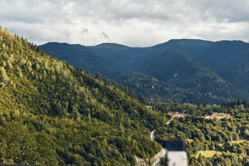 Majestic mountain landscape with a winding road threading through lush greenery under a cloudy sky, delivering a peaceful outdoor scene and expansive natural beauty