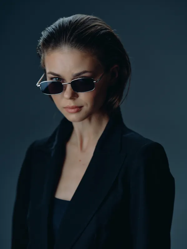 Stylish woman wearing black sunglasses and a dark blazer looking confidently ahead with a serious expression.