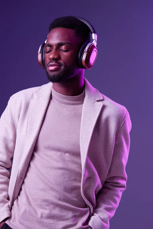 A young Black man wearing stylish headphones, enjoying music in a modern outfit in a vibrant purple setting, embodying relaxation and tranquility