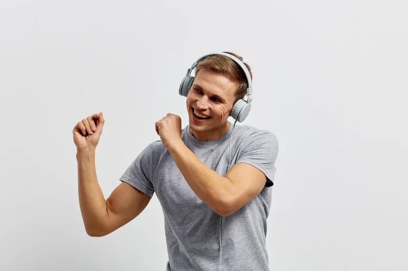 cheerful young caucasian man wearing headphones dancing listening music isolated on light gray background digital detox concept