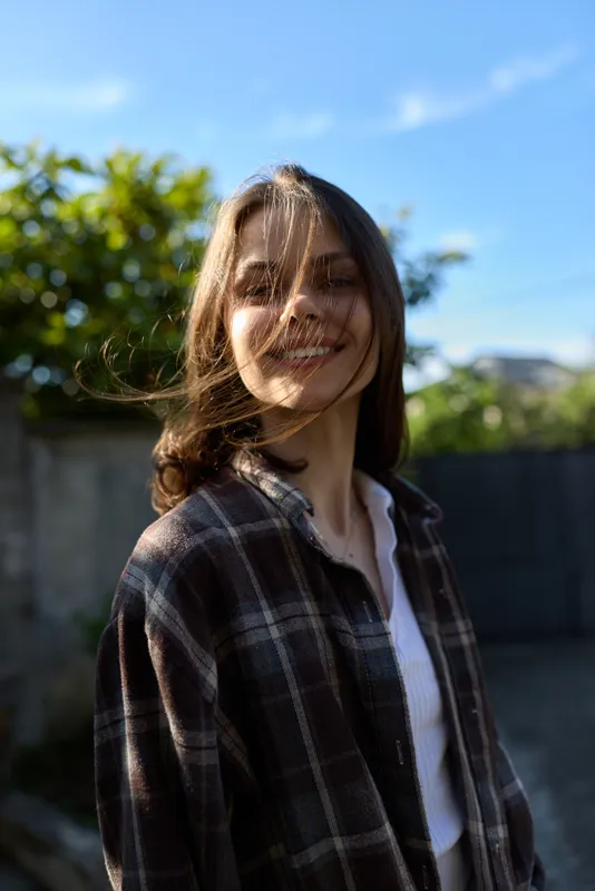 A smiling woman outdoors wearing a plaid shirt captures casual lifestyle and candid portrait, with bright natural light highlighting a relaxed mood in a sunny setting