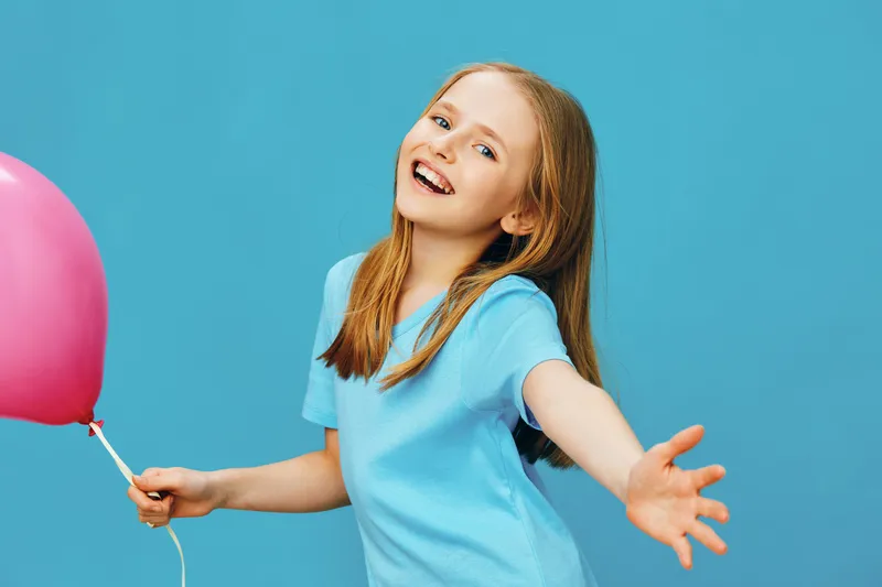 Happy girl with a pink balloon against a bright blue background, wearing a casual blue t shirt, radiating joy and playfulness, perfect for children s themes