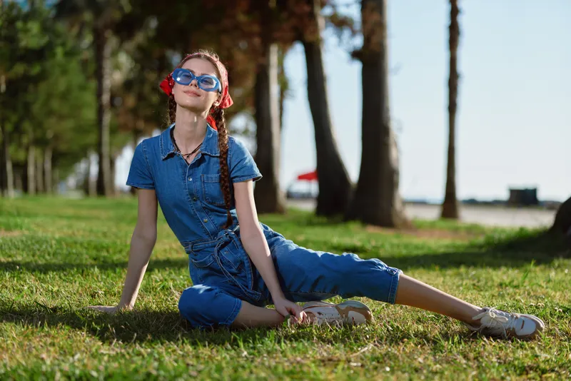 lifestyle woman in modern boho-western denim street style relaxing outdoors on grass with film color effect under bright natural light