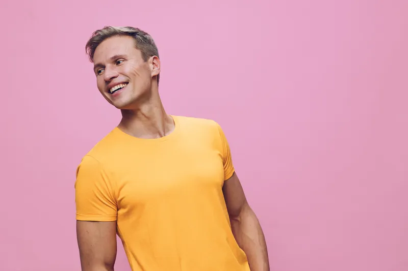 smiling man in orange t-shirt looking sideways isolated on pink background digital nomad lifestyle concept cheerful joyful casual young caucasian adult