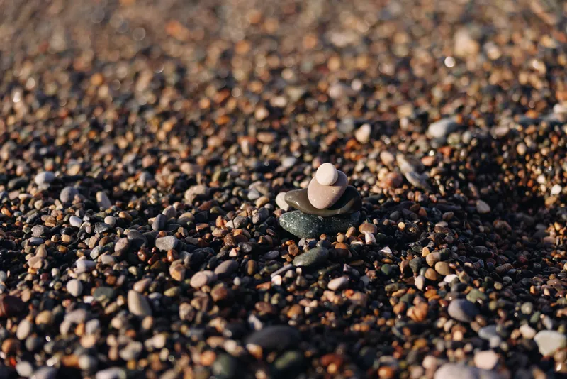 Small stone stack rests on a pebble beach, showcasing balance and calm in a natural outdoor scene with textured rocks and warm, gentle light.