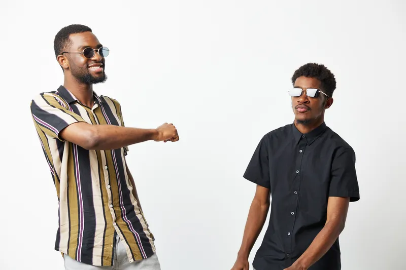 Two black men enjoying a fun moment together, showcasing joy and friendship. Their stylish outfits and playful expressions create an engaging atmosphere.