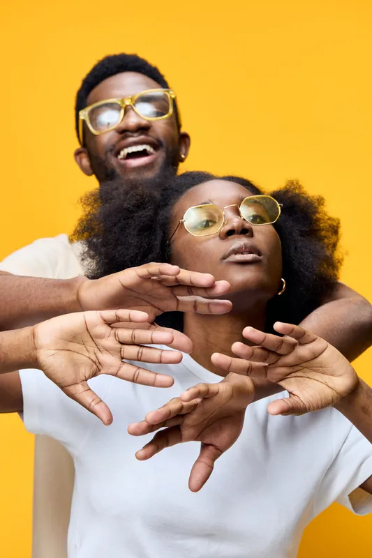 Happy couple with sunglasses posing against a bright yellow background, showcasing joy, confidence, and vibrant fashion in a creative portrait