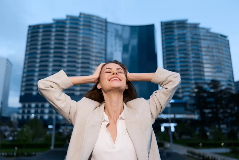 Confident businesswoman celebrating success outdoors in a modern urban setting with skyscrapers in the background, conveying professional empowerment and achievement.