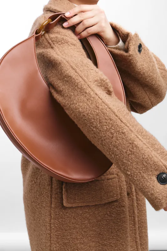 asian woman in a warm tan coat carries a stylish bag, presenting a modern fashion scene with soft textures and confident urban style.