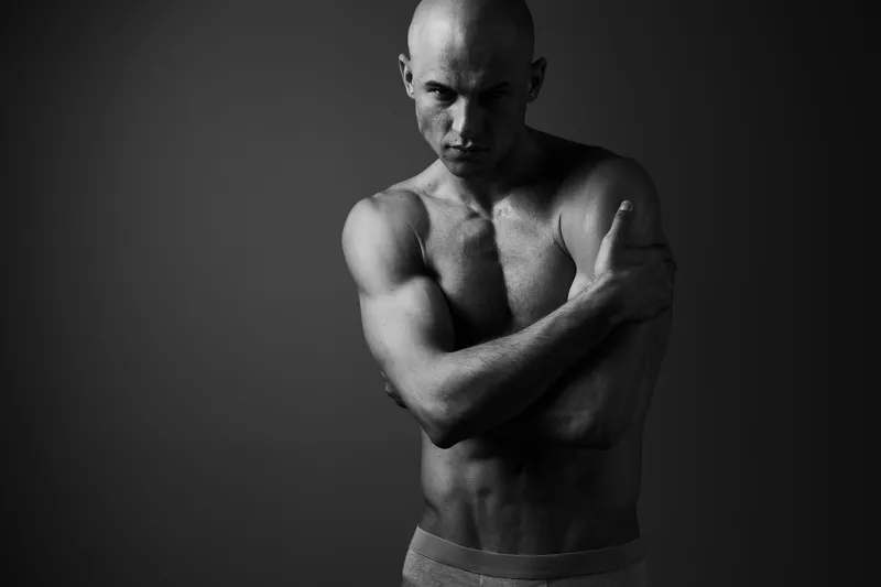 Black and white portrait of a man with a muscular build, showcasing strong emotions and a striking pose, creating an intense visual impact.