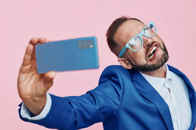 A professional man in a blue suit photographs himself with a confident smile against a vivid pink background, showcasing a modern business mood and isolated colorful backdrop.