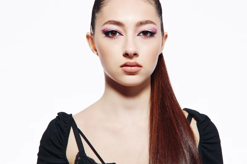 Young woman with smooth pale skin and long straight hair wears bold pink eyeshadow and natural lipstick on clean white background. Creative makeup concept for beauty and fashion.